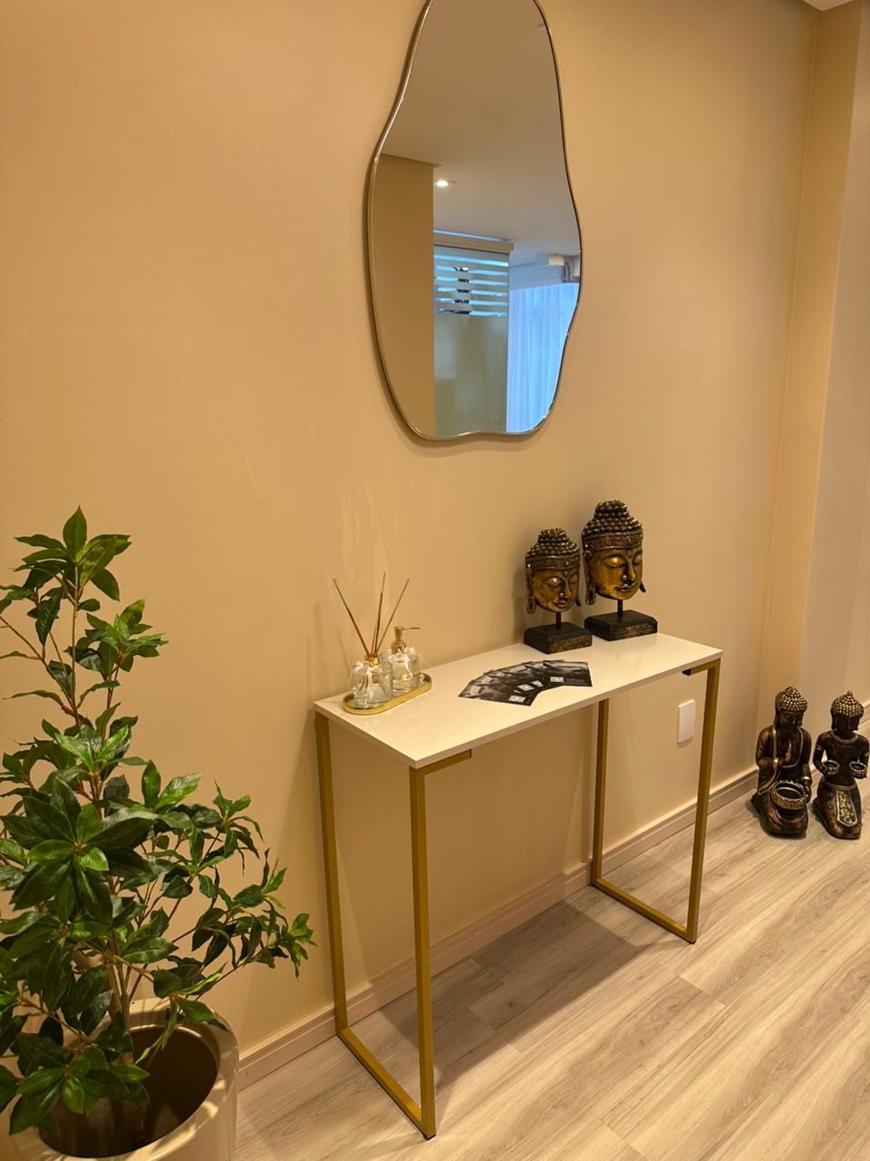 Recepção elegante com espelho orgânico e aparador dourado, Espaço Shanti